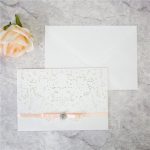 WEDINV142 Front of white lasercut pocket wedding invitation set with apricot ribbon bow and diamante